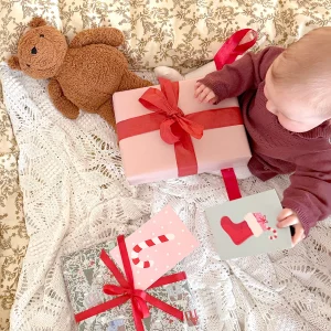 Baby som sitter å ser på julegaver med røde sløyfer og julekort på.