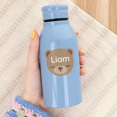 blå stålflaske med bjørne-navnelapp i en hånd med gul neglelakk