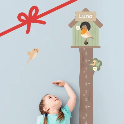 Barn som måler høyden sin ved en høydemåler formet som et tre med fuglehus og navnet “Luna”.