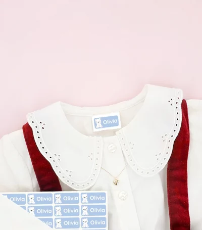 Barnesko og barnekjole med navnelapper plassert på klærne, omgitt av snøfnugg-dekor.