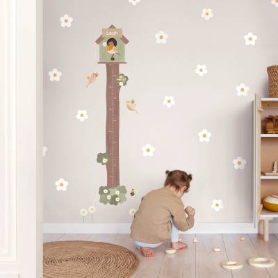 Barn ser på en veggdekor for barn med et naturmotiv og et måleverktøy. Dekoren inkluderer blomster og fugleillustrasjoner, som skaper en koselig atmosfære på barnerommet.