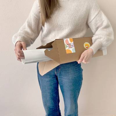 En person pakker ut en barneplakat fra en pappeske. Perfekt til barnerommet, plakaten har et lekent design som passer godt som veggdekor for barn.