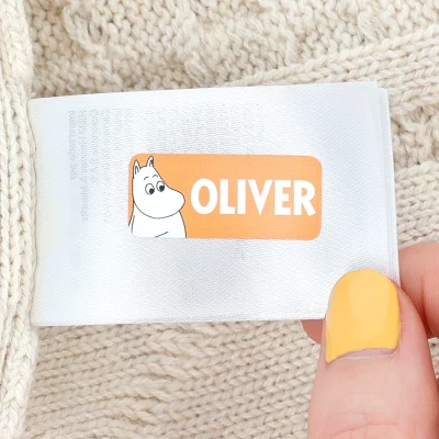 Navnelapp med navnet 'OLIVER' og en illustrasjon av Mummitrollet, festet på en ullgenser. Perfekt for å merke klær og tilbehør for barn.