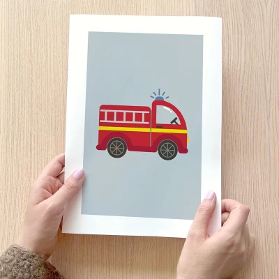 Alt-tekst: Hånd som holder en plakat med et illustrert rødt brannbil-design på en grå bakgrunn. Perfekt for veggdekor i barnerom eller som en del av en bursdagsfeiring.