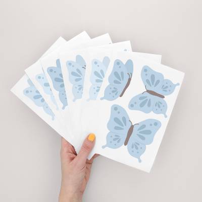 Hånd som holder ark med veggklistremerker med blå sommerfugldesign, perfekt for barnerom.