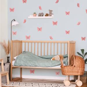 Et barnerom med en tremalt vugge og en grønt sengesett. Veggen er dekorert med rosa sommerfugler, som gir rommet et lekent preg.