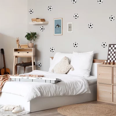 Alt-tekst: Stilig barnerom med moderne veggdekor av fotballer på grå bakgrunn. Rommet har en komfortabel seng med hvite puter og en koselig lendekappe. Det er også et skrivebord, en plante og en gitarkasse, samt lekekombinasjoner som sjakk og et keyboard. Dette er et perfekt miljø for barn som elsker fotball og kreativ lek.