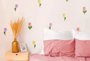 Interiørbilde av et barnerom med en vegg dekorert med fargerike blomstervegger. I forkant sees en blomsterpotte med tørkede blomster og en ramme med en illustrasjon. Bildet viser en koselig atmosfære og illustrerer hvordan veggdekor kan gi liv til et barnerom.