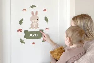 Mor viser barnet navnedekoren med en søt kanin og navnet Ava på veggen. Dekoren er omkranset av fallne blader og sopper, perfekt for å personifisere barnerommet. Dette designet gir et lekent preg og skaper en koselig atmosfære for små barn.