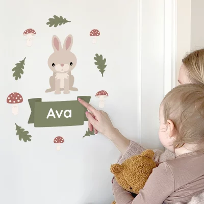 Mor viser barnet navnedekoren med en søt kanin og navnet Ava på veggen. Dekoren er omkranset av fallne blader og sopper, perfekt for å personifisere barnerommet. Dette designet gir et lekent preg og skaper en koselig atmosfære for små barn.