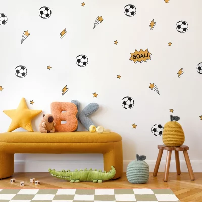 Et fargerikt barnerom med veggdekor av fotballer, lyn og stjerner. En gyllen sofa med flere lekne puter i form av stjerner og bokstaver kan sees, sammen med et leketøy og en grønnsakslignende figur. Dette er et perfekt rom for sportsinteresserte barn, med dekor som gir liv og glede til barnerommet.